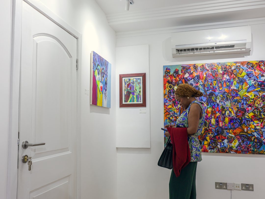 A visitor checking her phone beside a wall of paintings