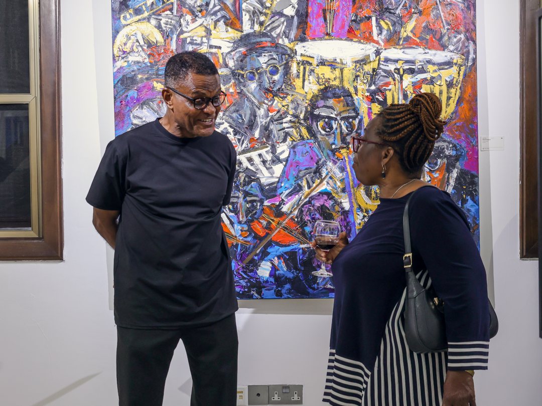 Two guests chatting in front of a painting of drummers