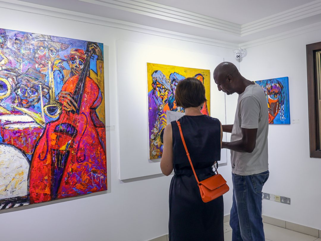 A couple reading the exhibition notes beside a painting of a double bass player